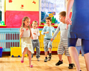 Group of children dancing together in a playroom in a nursery school.